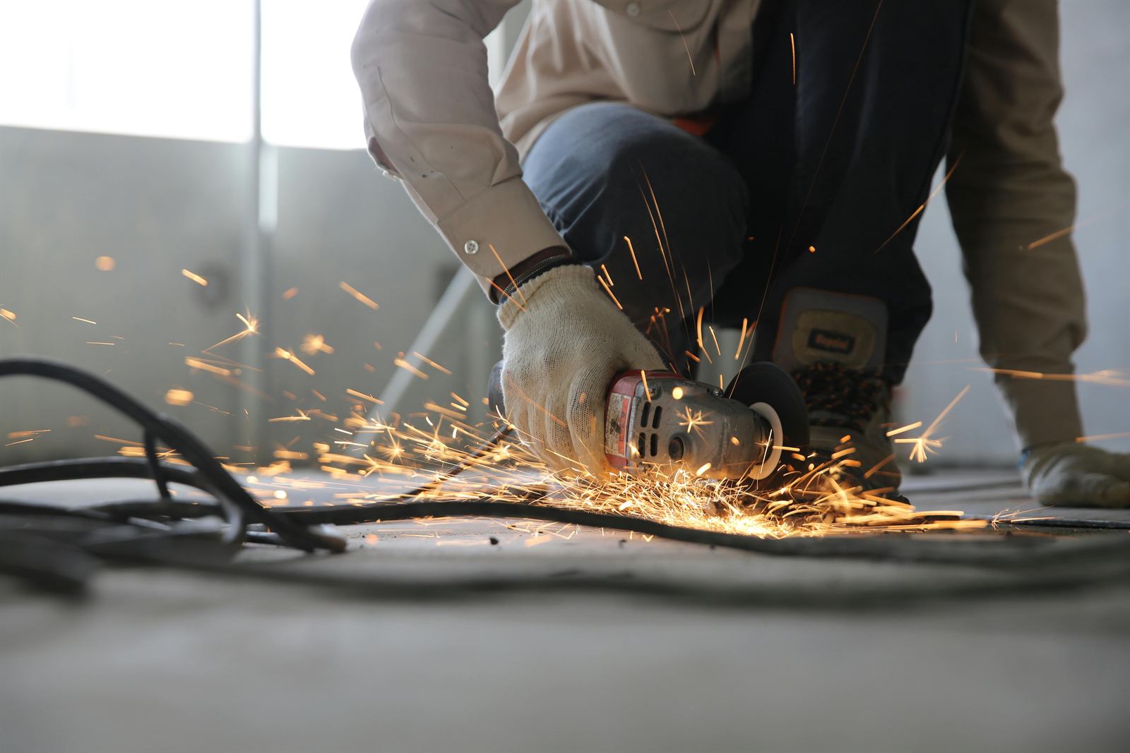 Worker in gloves cutting steel with an angle grinder, sparks spraying across the floor
